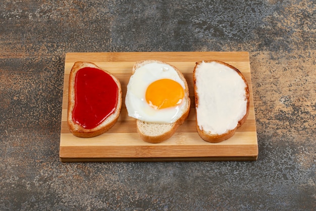 Toast with egg, cream cheese and jam on wooden board.