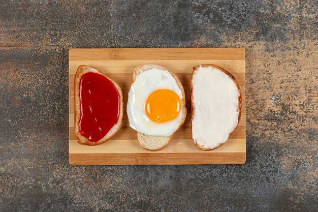 Toast with egg, cream cheese and jam on wooden board.