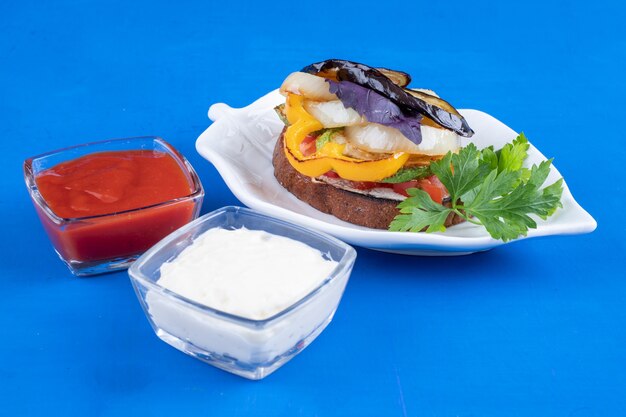 Toast with fried vegetables on leaf-shaped plate on blue surface