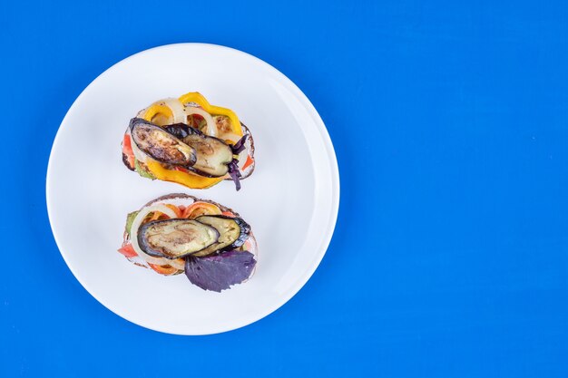 Toast with fried vegetables on white plate on blue surface. 