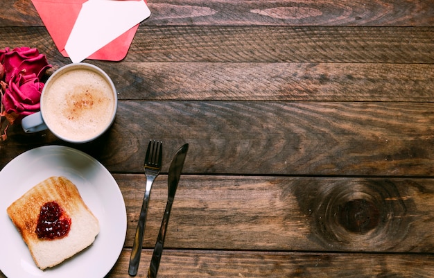 Free photo toast with jam on plate near cup of drink, flowers, envelope and cutlery