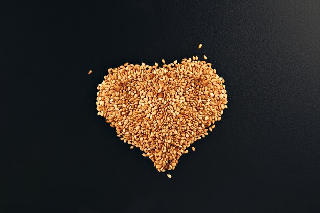 Toasted white sesame seeds arranged in a shape of heart on a smooth black table surface