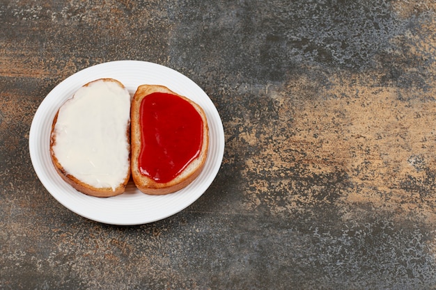 Toasts with strawberry jam and sour cream on white plate.