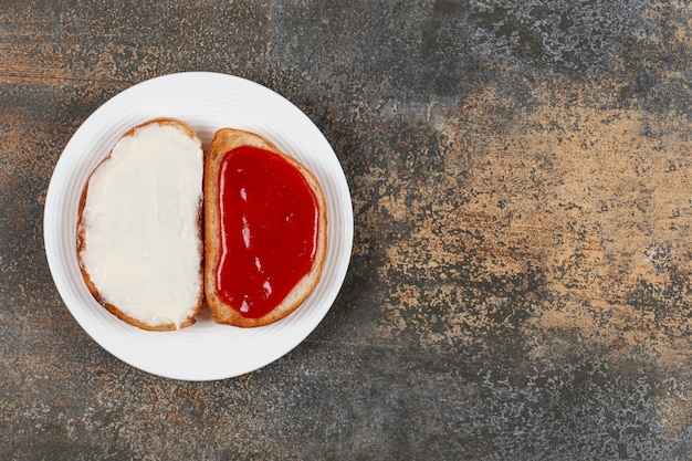 Toasts with strawberry jam and sour cream on white plate.