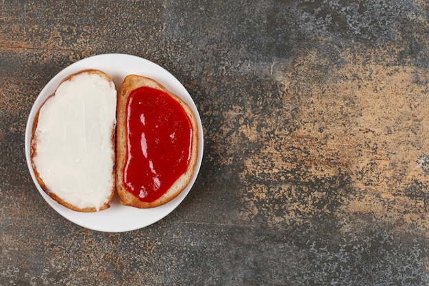 Toasts with strawberry jam and sour cream on white plate.