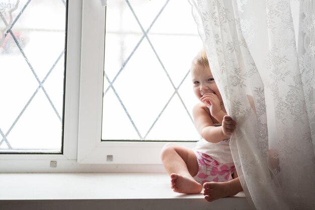 Toddler blonde girl plays on the window real interior lifestyle softfokus