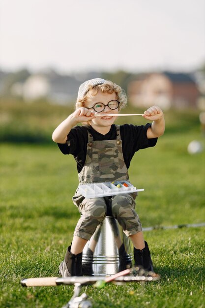 Toddler boy holding a box with a baits for fishing Boy wearing khaki overall Little boy sitting on a bucket