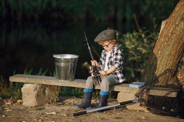 Toddler boy holding a fishing rod Boy wearing plaid shirt and a hat Little boy fishing on summer