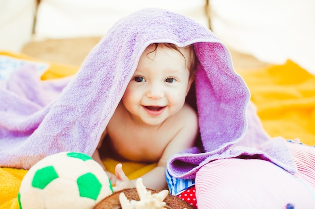 "Toddler boy lying covered with purple towel"