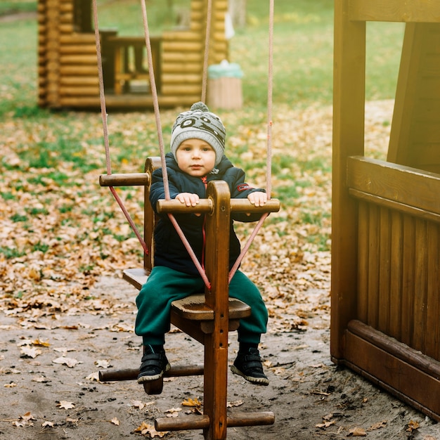 Toddler boy on swing in autumn garden