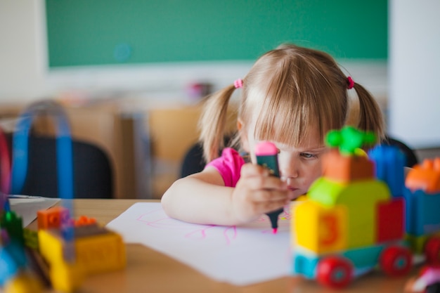 Toddler girl drawing on paper in classroom