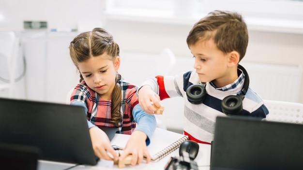 Toddlers playing with wooden blocks with laptop on desk