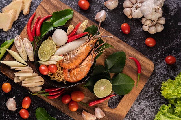 Tom Yum Kung in a bowl with tomato, chili, lemongrass, garlic, lemon, and kaffir lime leaves