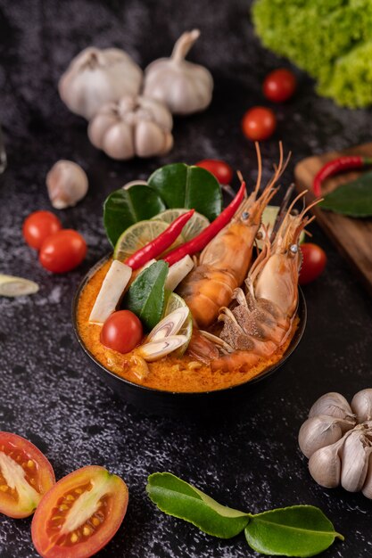 Tom Yum Kung in a bowl with tomato, chili, lemongrass, garlic, lemon, and kaffir lime leaves