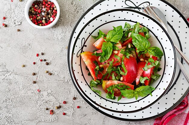 Tomato salad with basil and pine nuts in bowl - healthy vegetarian vegan diet organic food appetizer. Top view. Flat lay