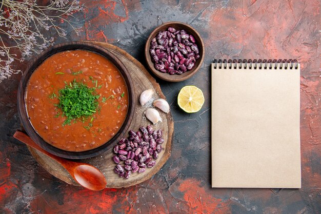 Tomato soup beans garlic on wooden cutting board spoon and notebook on mix color table