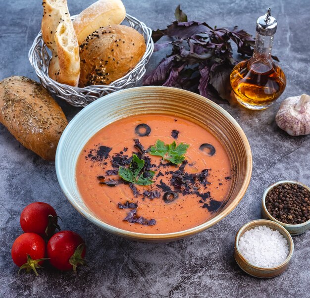 Tomato soup bowl garnished with olive dark basil leaves and parsley