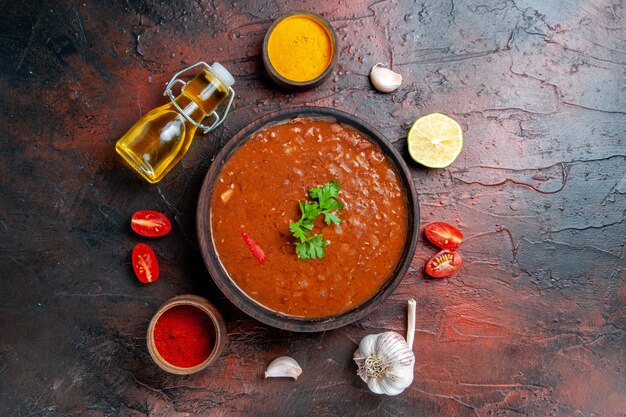 Tomato soup in a brown bowl and different spices garlic lemon on mixed color table 