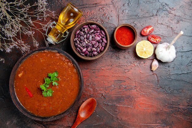 Tomato soup in a brown bowl pepper garlic lemon and beans on mixed color table