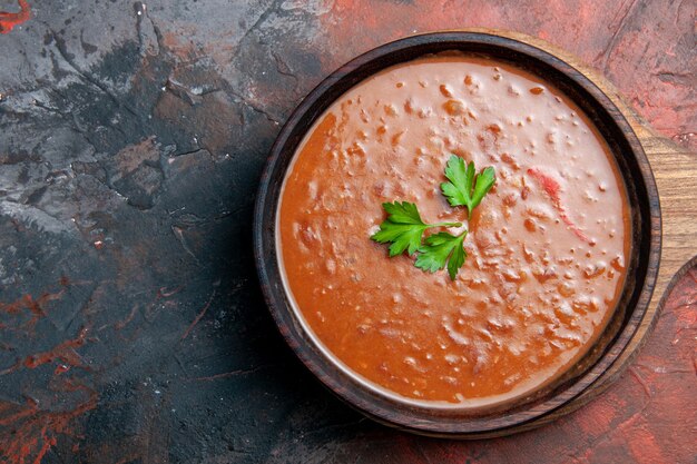 Tomato soup on a brown cutting board on the right side of a mixed color table