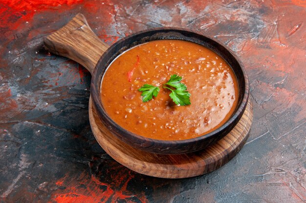 Tomato soup on a brown cutting board on the right side of a mixed color table