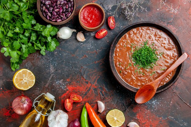 混合色のテーブルに緑のオイルボトルにんにくとスプーンの束とトマトスープ