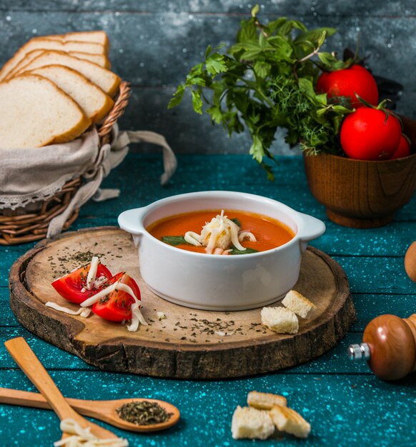 Tomato soup with parmesan on a piece of woode with tomatoes and crackers around.