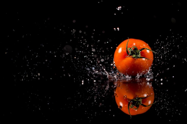 The tomato with drops stands on the black background