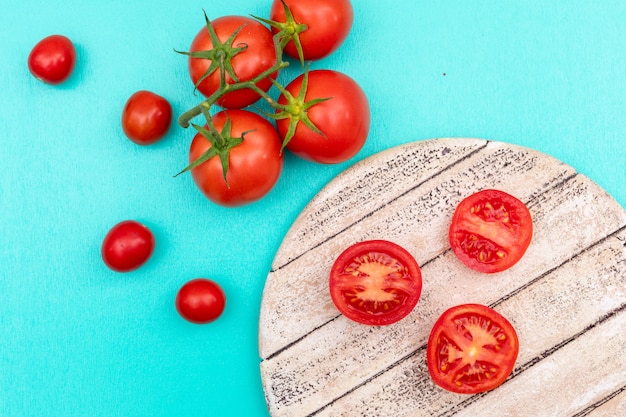 Tomato on wooden board branch of cherry tomato on blue surface top view