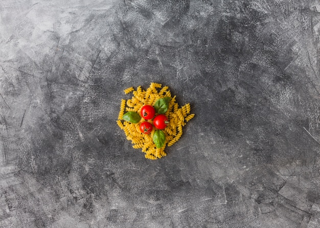 Tomatoes and basil leaves over the raw fusilli on dirty stain background