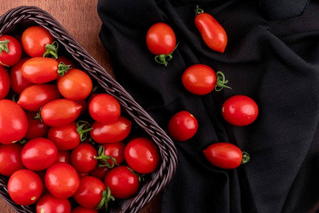 Tomatoes in basket near the cherry tomato top view on black cloth