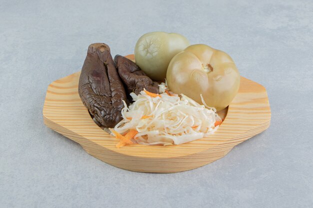 Tomatoes, eggplants and sauerkraut in a wooden plate on the marble surface