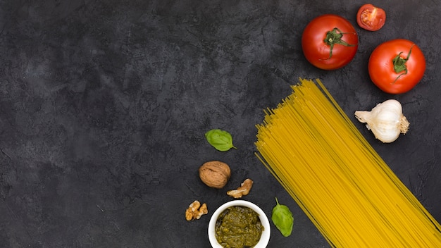Free photo tomatoes; garlic bulb; basil; walnuts; sauce and spaghetti on black textured backdrop