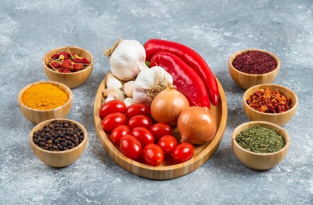 Tomatoes, garlic and peppers on wooden plate with spices. 