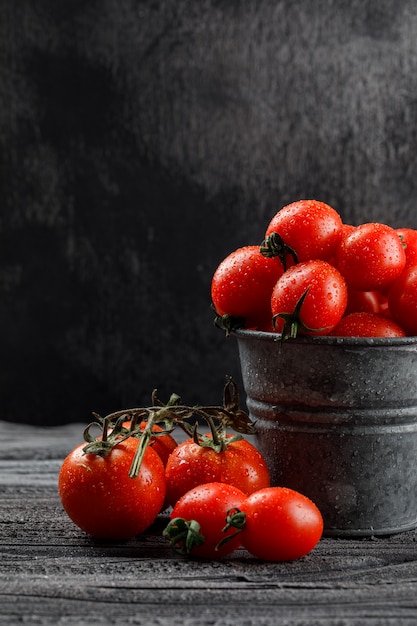 Pomodori in una vista laterale del mini secchio sulla parete di legno e scura grigia