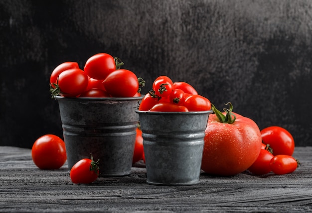 Tomatoes in mini buckets on grey wooden and grungy wall. side view.