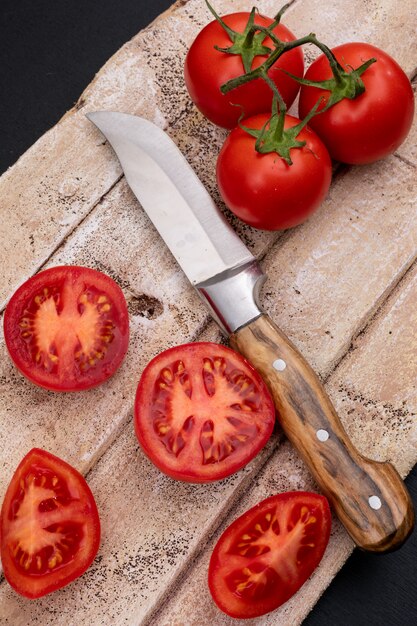 Tomatoes near the knife top view on wooden cutting board on dark surface