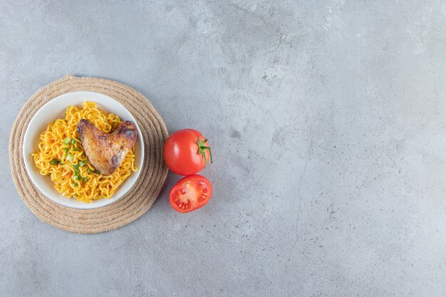 Tomatoes and noodle bowl on a trivet, on the marble background. 