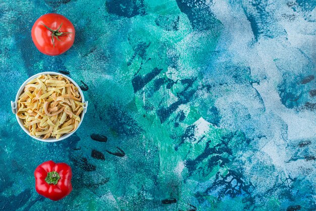 Tomatoes, pepper and homemade noodle in a bucket , on the blue background. 