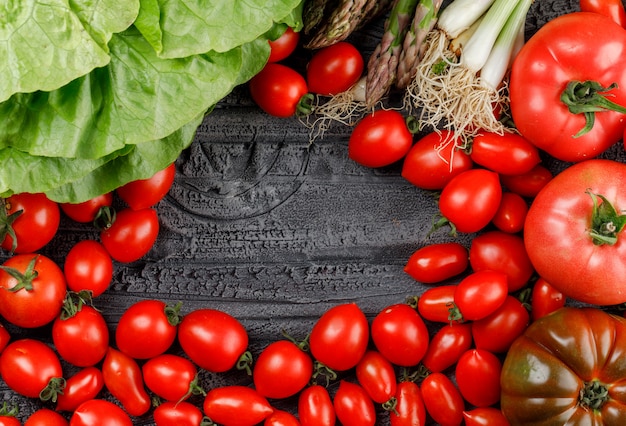 Tomatoes pile with lettuce, asparagus, green onions flat lay on a grey wooden wall