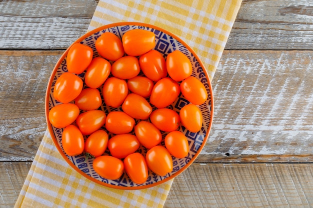 Tomatoes in a plate on wooden and kitchen towel, flat lay