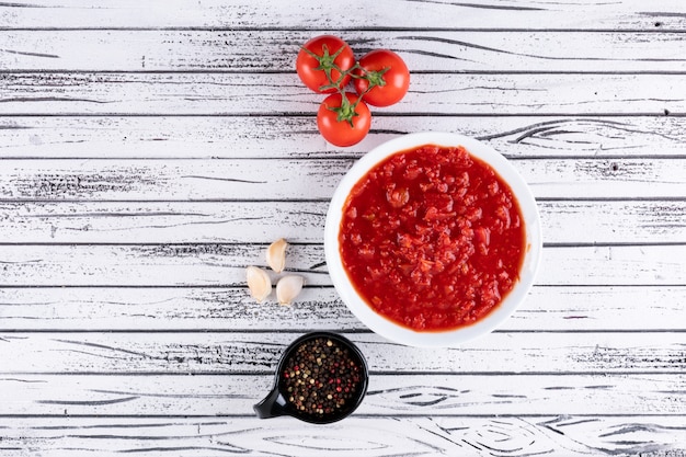 Foto gratuita pomodori e salsa al pomodoro in polvere bianca del pepe nero della ciotola in ciotola nera su superficie di legno bianca