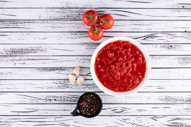 Tomatoes and tomato sauce in white bowl black pepper powder in black bowl on white wooden surface