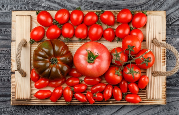 Varietà di pomodori in un vassoio fatto a mano rustico su una parete grigia in legno. disteso.