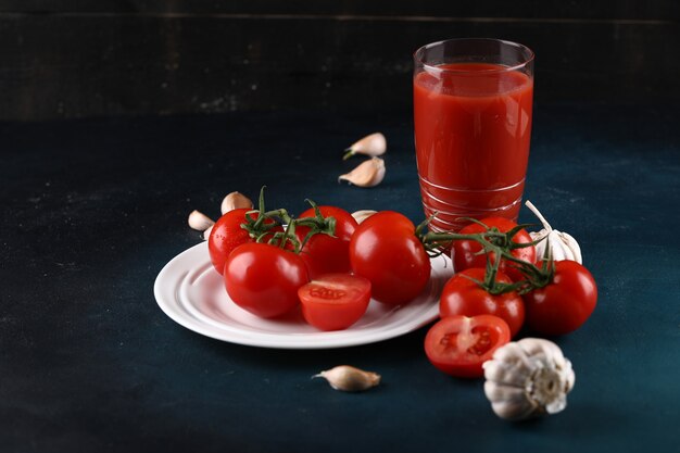 Tomatoes in white plate with garlic gloves and a glass of tomato juice.