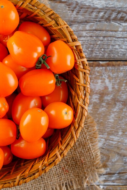 Tomatoes in a wicker basket on wooden and piece of sack. close-up.