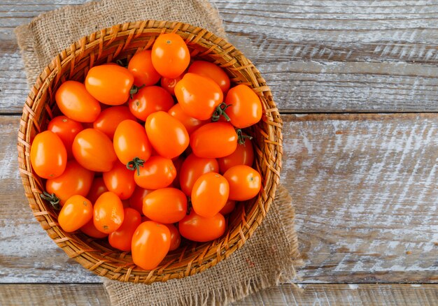 Tomatoes in a wicker basket on wooden and piece of sack. flat lay.