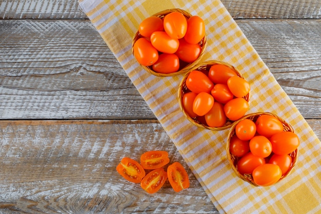 Tomatoes in wicker baskets on wooden and kitchen towel. flat lay.