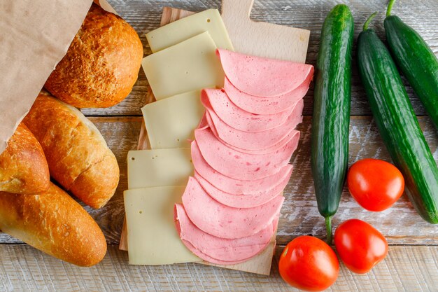 Tomatoes with bread, cheese, sausage, cucumbers flat lay on a wooden table