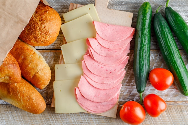 Tomatoes with bread, cheese, sausage, cucumbers flat lay on a wooden table